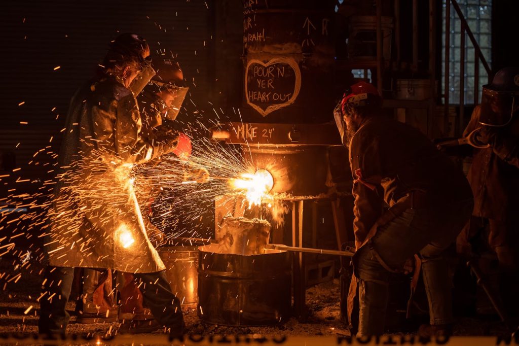 Industrial workers pouring molten metal with sparks flying in Milwaukee workshop.